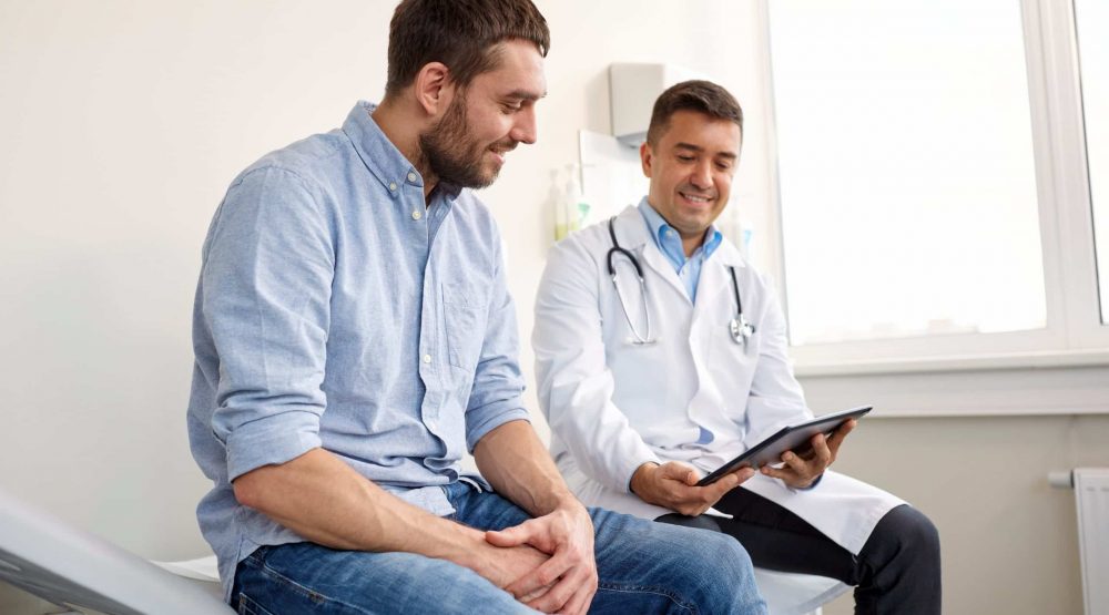 medicine, healthcare and people concept - smiling doctor with tablet pc computer and young man patient meeting at hospital